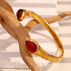 Close-up of snake bangle with red stones and hammered texture on vintage wood