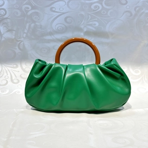 Detail of green ruched cloud bag featuring a round brown resin handle on white fabric