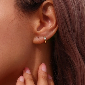 Gros plan d'une boucle d'oreille créole dorée sertie d'un zircon rectangulaire sur l'oreille