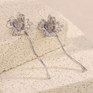 Detailed macro view of silver flower-shaped long drop earrings on stone background