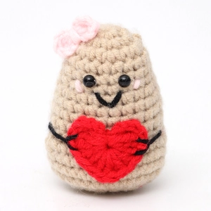 Close-up of handmade crochet potato toy with pink bow and heart decor on white background