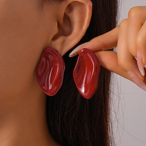 Close-up of a model wearing deep red irregular drop earrings with glossy resin finish