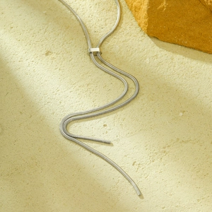 Minimalist silver long snake chain tassel necklace on natural stone textured background
