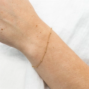 Close-up of a gold beaded silver chain bracelet worn on a wrist with linen background