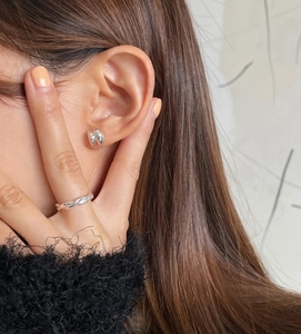 Close-up of minimalist silver bean earrings and twisted ring worn on a model with black knitwear