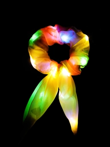 Close-up of rainbow gradient LED scrunchie glowing with internal lights on dark background