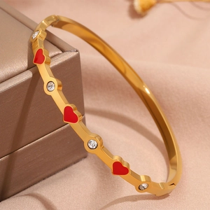 Dettaglio del bracciale in titanio dorato con cuori in smalto rosso e strass rotondi