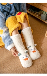 Detailed view of white coral fleece slippers with cute duck design on a cozy rug