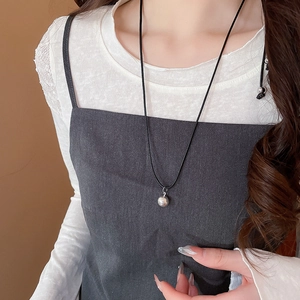 Silver ball pendant on a black cord necklace styled with a white and grey outfit