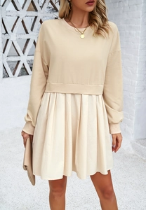 Détail d'une robe beige à manches longues avec patchwork contrasté et jupe plissée