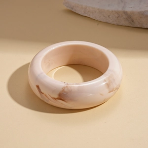 Detailed view of pink resin bangle with dark marble texture on warm beige background