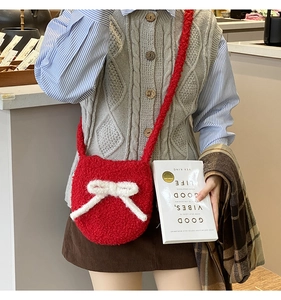 Red plush crossbody bag with a white bow detail shown on a model in a cozy setting