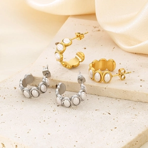 Detail of gold and silver C-shaped earrings with pearls on a textured stone surface