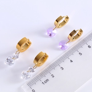 Detail view of gold hoop earrings with white and purple zircon drops next to a scale