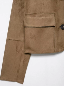 Detail der braunen Wildlederjacke mit aufgesetzter Tasche, schwarzem Knopf und Nähten