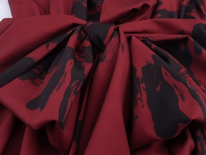 Detail des eleganten roten Knotendesigns und des schwarzen Pinselstrichdrucks am Kleid