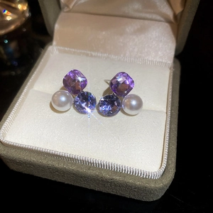 Detail shot of sparkling purple crystal and white pearl bow earrings on velvet tray