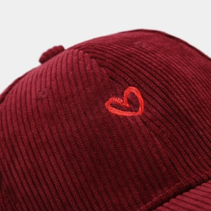 Detailed macro view showing corduroy texture and red heart embroidery on the burgundy cap