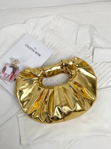 Detailed macro view of the gold metallic pleated texture and knotted handle on this bag