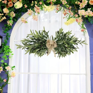 Artificial olive branch wreath with burlap bow hanging on a white arched window frame