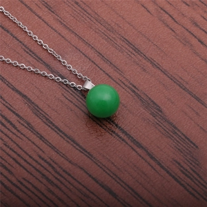 Detail of a minimalist silver chain necklace featuring a smooth green round bead pendant