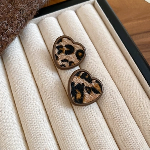 Macro detail of heart-shaped leopard print earrings in a soft cream velvet jewelry box