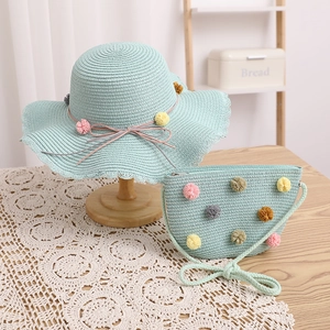 Detail of mint green straw sun hat and matching crossbody bag with colorful pom-poms