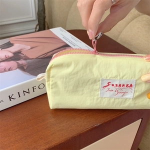 Detail of yellow nylon pencil case with pink zipper and minimalist logo label on wood