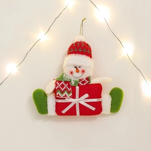 Cute plush snowman Christmas ornament with red knit hat and gift box on warm light background