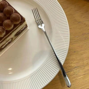 Polished stainless steel fruit fork set on tiramisu dessert plate in professional top view