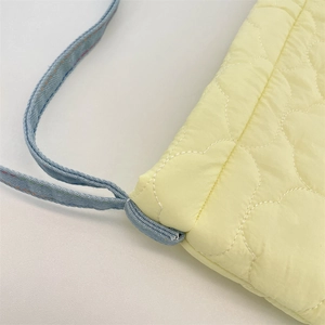 Close-up of yellow quilted bag with heart stitching and blue woven strap detail