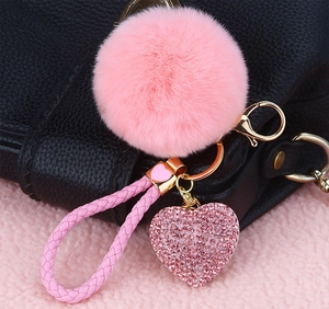 Pink faux fur pompom keychain with crystal heart pendant and woven strap on a black bag