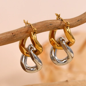 Two-tone interlocking link earrings in gold and silver finish hanging on a wooden branch