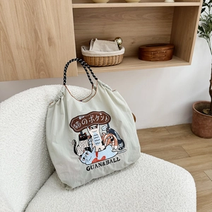 Close-up of light grey nylon tote bag with cute cat illustration on a cozy sofa chair
