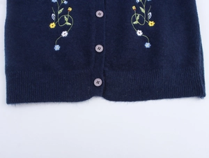 Detail of navy knit cardigan featuring colorful floral embroidery and round buttons