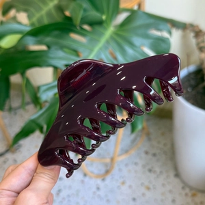 Large dark purple translucent resin hair claw clip shown in hand with a natural leaf background