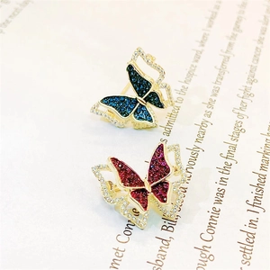 Close-up of butterfly brooches with blue and red zircons on a textured paper background