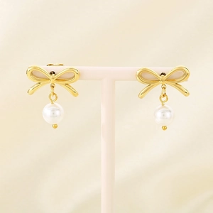 Detail of gold bow earrings with a white pearl drop displayed on a white stand