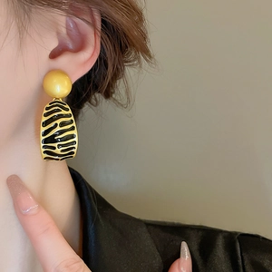 Close-up of model wearing geometric striped enamel earring with animal print and gold ball