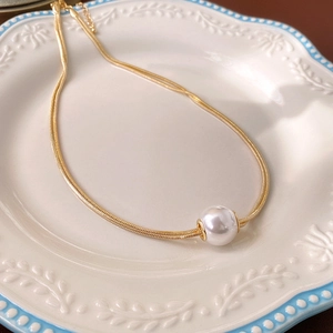 Detailed close-up of golden snake chain necklace with a pearl pendant on a white ceramic plate