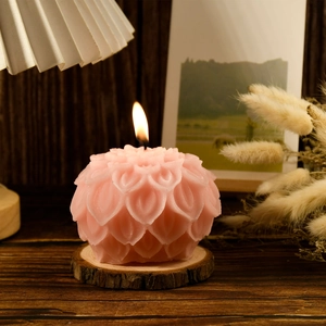 Detailed view of a pink lotus-shaped scented candle lit on a natural wood slice base