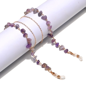 Detail of amethyst beads on gold chain strap for glasses wrapped on white cylinder