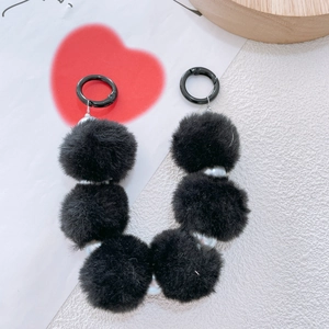 Close-up of black plush pompom and pearl bead keychain charm on card background