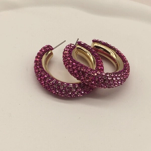 Close-up of gold hoop earrings featuring dense pink rhinestone pavé and thick design