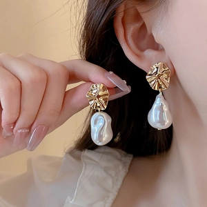 Close-up of gold star earrings with large baroque pearls worn by a female model