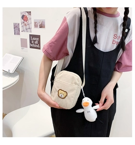 Detail of beige corduroy crossbody bag with bear embroidery and plush duck charm accessory
