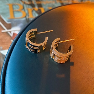 Detail of gold-plated asymmetric C-shaped earrings with clear crystals on a dark surface