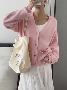 Detail view of pink V-neck knit cardigan featuring gold buttons and front pockets