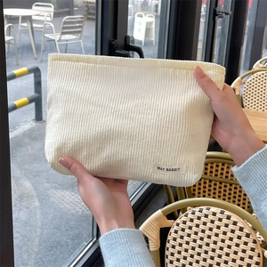 Detail of a creamy corduroy makeup bag held in hand, showing fine ribbed texture and tag
