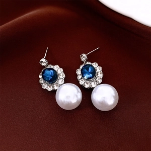 Detail of silver drop earrings featuring a deep blue gem surrounded by crystals and a pearl